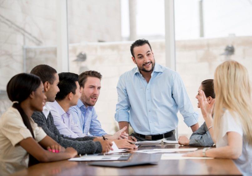 A multi-ethnic group of business associates having a discussion at work during a meeting in a room with natural light.