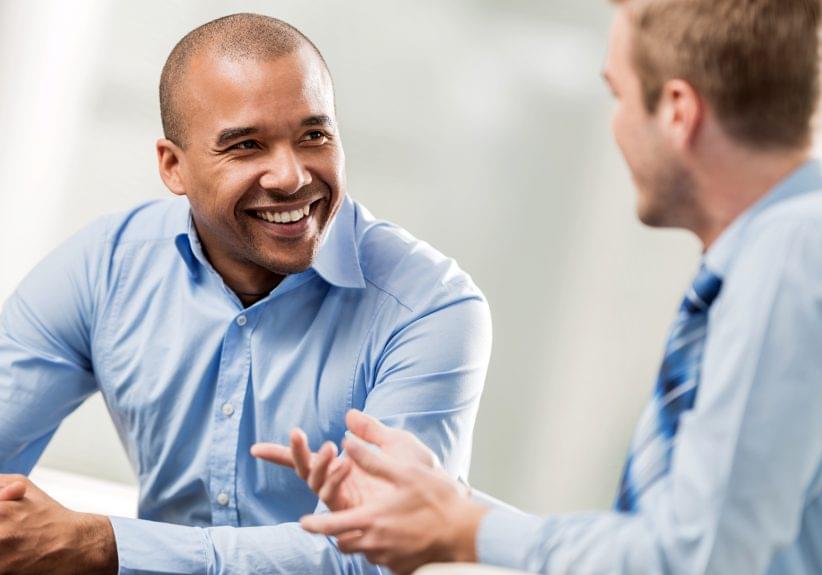 Two businessmen sitting in the office and communicating. Focus is on happy African American businessman.